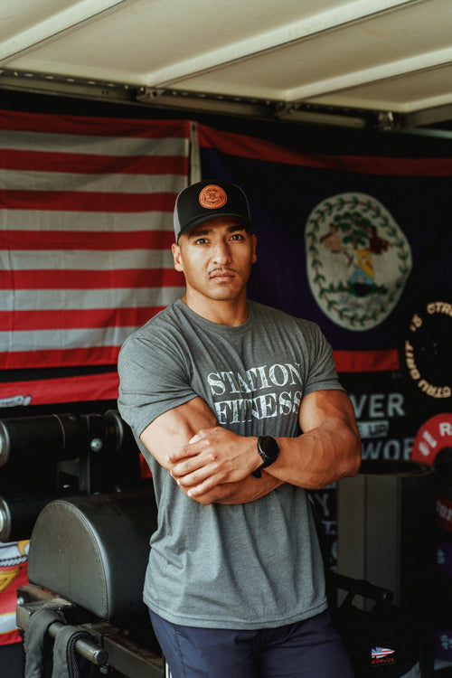 Man wearing Station Fitness Logo Hat in front of American flag in gym setting
